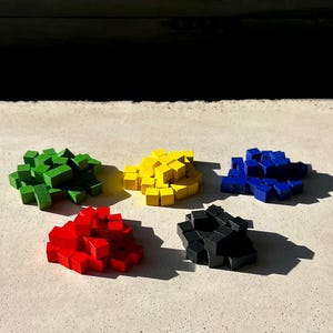 Può includere: Cinque pile di piccoli cubi di legno colorati. I cubi sono disposti in cerchio, con cubi rossi, verdi, gialli, blu e neri in ogni pila.
