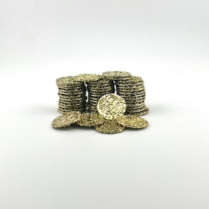 May include: A collection of gold-colored coins, some stacked in piles and others scattered. The coins have intricate designs and are arranged against a white background. The coins appear to be made of metal and have a slightly aged appearance.