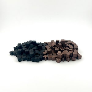 May include: A collection of small, dark brown and black square blocks. The blocks are scattered on a white surface. The dark brown blocks are a solid color, while the black blocks have a porous texture.