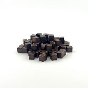 May include: A pile of small, dark brown, square cubes. The cubes are evenly sized and appear to be made of a solid material. The cubes are scattered on a white surface.
