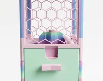 May include: A pastel-colored claw machine featuring a rainbow gradient frame, a hexagonal grid pattern on the upper enclosure, a light green storage drawer with a pink handle, and a pink dispensing chute at the base for small items.