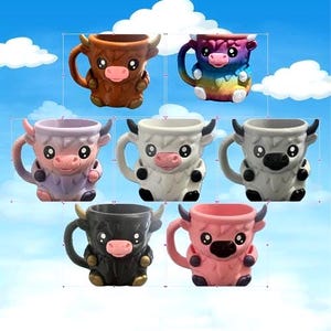 May include: A selection of ceramic Highland cow mugs in various colours: brown, rainbow, lavender, white, grey, black, and pink. Each mug has horns, a pink nose, and large eyes. These mugs are designed to resemble the Scottish breed.