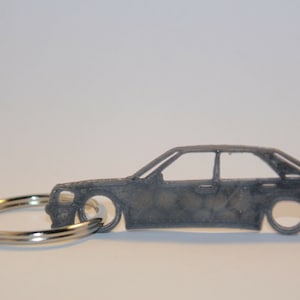 以下が含まれることがあります： 車の詳細なシルエットが刻まれた銀色の金属製のキーホルダー。キーホルダーには銀色の金属製のリングが付いています。