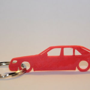 May include: A red plastic car keychain. The car is a sedan with a detailed silhouette. The keychain is attached to a silver metal ring.
