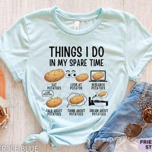 Puede incluir: Una camiseta azul claro con el texto "Things I do in my spare time" y una serie de ilustraciones de patatas con diferentes actividades, como comer, mirar, investigar, hablar, pensar y soñar con patatas.