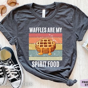 Pu&ograve; includere: T-shirt grigio scuro melange con la scritta "WAFFLES ARE MY SPIRIT FOOD" e una grafica di waffle con sciroppo. Il design presenta una combinazione di colori retr&ograve; ed &egrave; stampato su una maglietta morbida.