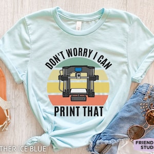 May include: Light blue t-shirt with a retro-style graphic of a 3D printer and the text "Don't Worry I Can Print That".