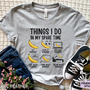 Peut inclure: Un t-shirt gris avec le texte "Things I do in my spare time" et une s&eacute;rie d'illustrations de bananes avec du texte sur le fait de manger, de regarder, de rechercher, de parler, de penser et de r&ecirc;ver de bananes.