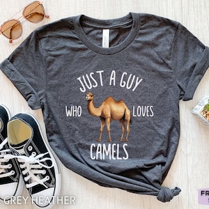 May include: Dark grey heather t-shirt with the text "Just a guy who loves camels" and a camel illustration. The shirt is paired with black sneakers and sunglasses.