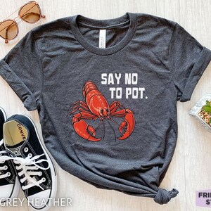 Puede incluir: Una camiseta de color gris oscuro jaspeado con un gráfico de langosta roja y el texto "Say No To Pot."