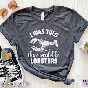 May include: Dark grey heather t-shirt with a white graphic of a lobster and the text "I was told there would be lobsters".