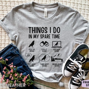 K&ouml;nnte beinhalten: Graues T-Shirt mit dem Text "Things I do in my spare time" und einer Liste von Aktivit&auml;ten, die mit Kr&auml;hen zu tun haben. Die Aktivit&auml;ten umfassen: Kr&auml;hen f&uuml;ttern, Kr&auml;hen beobachten, Kr&auml;hen recherchieren, &uuml;ber Kr&auml;hen sprechen, an Kr&auml;hen denken und von Kr&auml;hen tr&auml;umen.