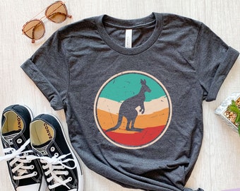 May include: A dark grey heather short-sleeve t-shirt featuring a circular graphic with a distressed finish. The graphic depicts a silhouette of a kangaroo against a background of horizontal stripes in teal, beige, orange, and red colors.