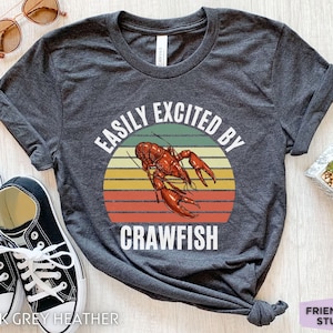 Op de afbeelding: Donkergrijs heather t-shirt met een vintage-stijl grafische afbeelding van een rivierkreeft en de tekst "Easily Excited By Crawfish".