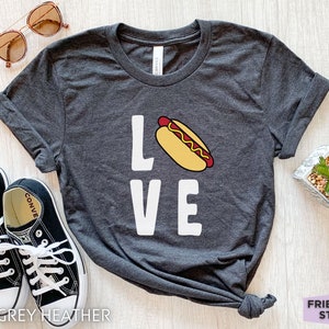 May include: Dark grey heather t-shirt with a white graphic of a hot dog and the word "LOVE".