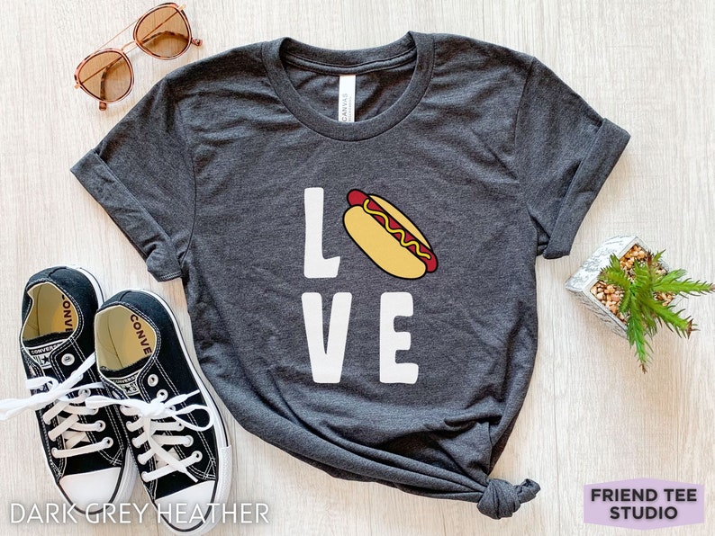 May include: Dark grey heather t-shirt with a white graphic of a hot dog and the word "LOVE".