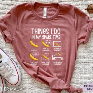 Peut inclure: Un t-shirt en mauve bruy&egrave;re avec le texte "THINGS I DO IN MY SPARE TIME" et une liste d'activit&eacute;s li&eacute;es aux bananes. Les activit&eacute;s comprennent "EAT BANANAS", "LOOK AT BANANAS", "RESEARCH BANANAS", "TALK ABOUT BANANAS", "THINK ABOUT BANANAS", et "DREAM ABOUT BANANAS".