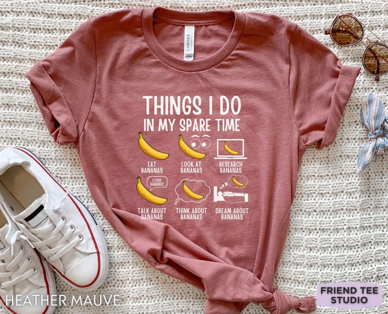 Peut inclure: Un t-shirt en mauve bruy&egrave;re avec le texte "THINGS I DO IN MY SPARE TIME" et une liste d'activit&eacute;s li&eacute;es aux bananes. Les activit&eacute;s comprennent "EAT BANANAS", "LOOK AT BANANAS", "RESEARCH BANANAS", "TALK ABOUT BANANAS", "THINK ABOUT BANANAS", et "DREAM ABOUT BANANAS".