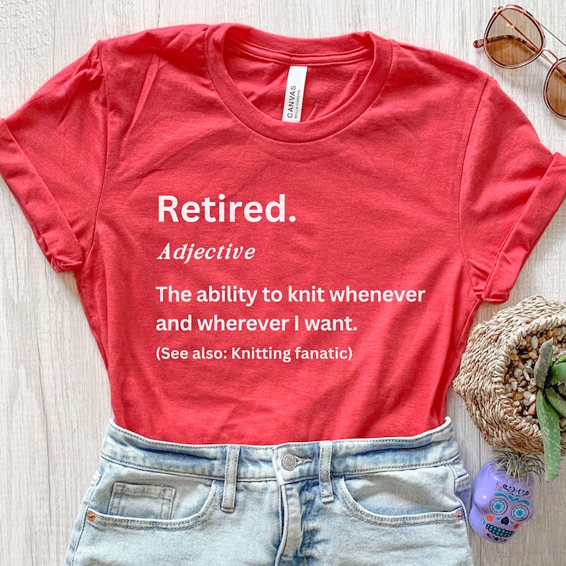 Puede incluir: Una camiseta roja con la palabra "Retired" impresa en blanco, junto con una definici&oacute;n sobre tejer. La camiseta se combina con pantalones cortos de mezclilla y gafas de sol, lo que sugiere un estilo casual y relajado.