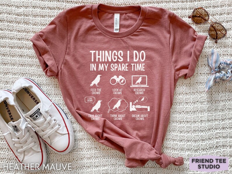 K&ouml;nnte beinhalten: Ein T-Shirt in Heide-Mauve mit einer wei&szlig;en Grafik, auf der "Things I do in my spare time" steht und Aktivit&auml;ten im Zusammenhang mit Kr&auml;hen aufgelistet sind.