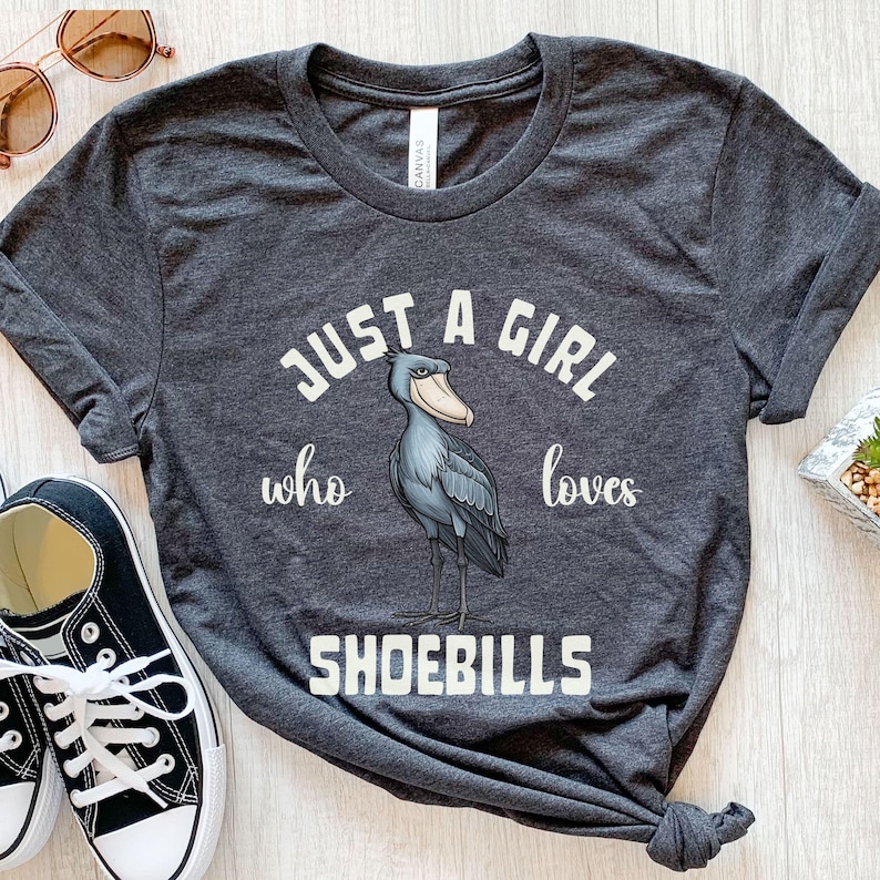Puede incluir: Camiseta gris oscuro con un gr&aacute;fico blanco de un picozapato y el texto "Just a girl who loves shoebills".