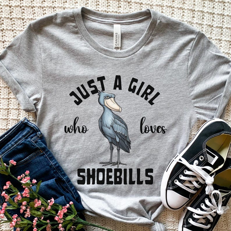 Puede incluir: Camiseta gris con una ilustraci&oacute;n de dibujos animados de un zoc&oacute; y el texto "Just a girl who loves shoebills".
