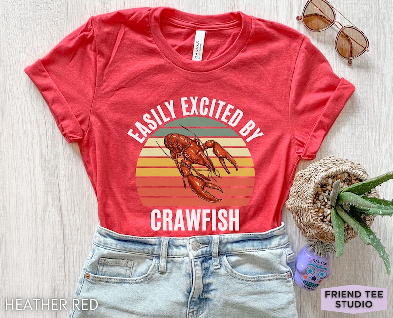 Op de afbeelding: Rood T-shirt met een vintage-stijl grafische afbeelding van een rivierkreeft en de tekst "Easily Excited By Crawfish".