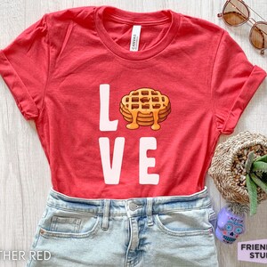 K&ouml;nnte beinhalten: Rotes T-Shirt mit dem Wort "LOVE" in wei&szlig;er Schrift. Das "O" ist durch ein Cartoon-Bild eines Waffels mit Sirup ersetzt.