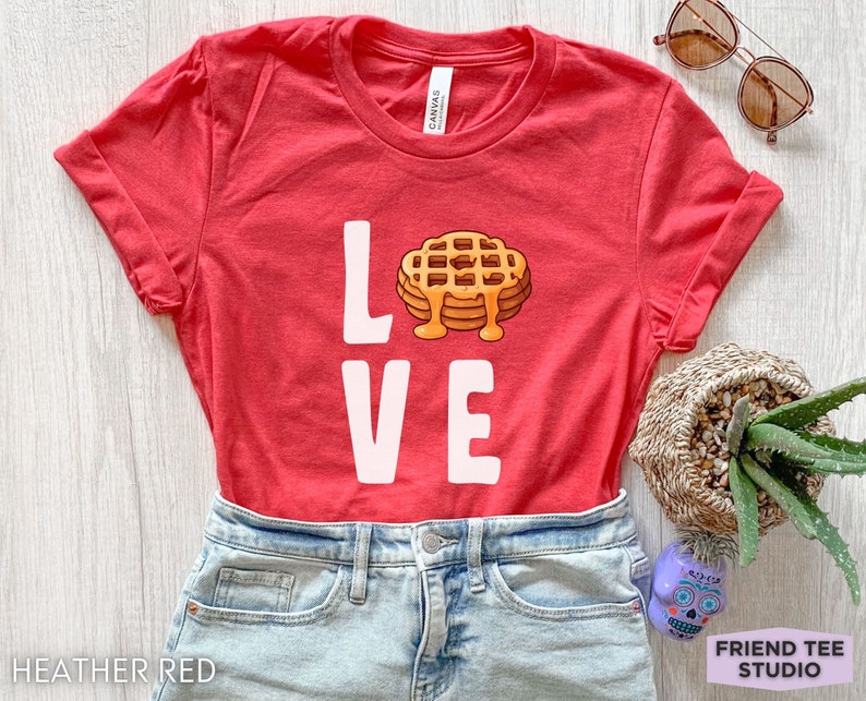 K&ouml;nnte beinhalten: Rotes T-Shirt mit dem Wort "LOVE" in wei&szlig;er Schrift. Das "O" ist durch ein Cartoon-Bild eines Waffels mit Sirup ersetzt.