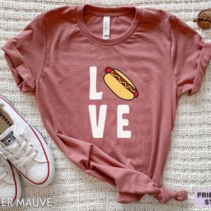 May include: A heather mauve t-shirt with a white graphic of a hot dog and the word "LOVE".