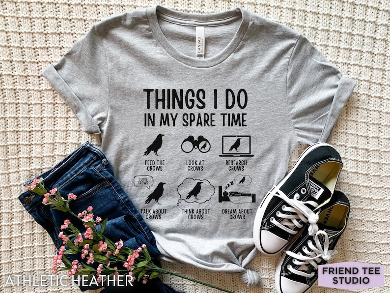 K&ouml;nnte beinhalten: Graues T-Shirt mit dem Text "Things I do in my spare time" und einer Liste von Aktivit&auml;ten, die mit Kr&auml;hen zu tun haben. Die Aktivit&auml;ten umfassen: Kr&auml;hen f&uuml;ttern, Kr&auml;hen beobachten, Kr&auml;hen recherchieren, &uuml;ber Kr&auml;hen sprechen, an Kr&auml;hen denken und von Kr&auml;hen tr&auml;umen.