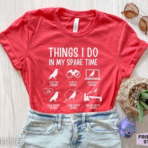 K&ouml;nnte beinhalten: Rotes T-Shirt mit wei&szlig;em Text, der "Things I do in my spare time" lautet. Der Text ist von Illustrationen von Kr&auml;hen und Aktivit&auml;ten im Zusammenhang mit Kr&auml;hen umgeben, wie z. B. Kr&auml;hen f&uuml;ttern, Kr&auml;hen beobachten, Kr&auml;hen erforschen, &uuml;ber Kr&auml;hen sprechen, &uuml;ber Kr&auml;hen nachdenken und von Kr&auml;hen tr&auml;umen.