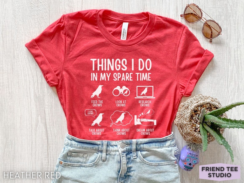 K&ouml;nnte beinhalten: Rotes T-Shirt mit wei&szlig;em Text, der "Things I do in my spare time" lautet. Der Text ist von Illustrationen von Kr&auml;hen und Aktivit&auml;ten im Zusammenhang mit Kr&auml;hen umgeben, wie z. B. Kr&auml;hen f&uuml;ttern, Kr&auml;hen beobachten, Kr&auml;hen erforschen, &uuml;ber Kr&auml;hen sprechen, &uuml;ber Kr&auml;hen nachdenken und von Kr&auml;hen tr&auml;umen.