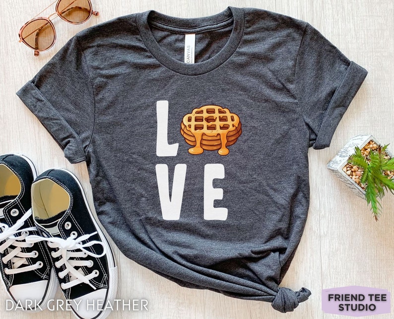 K&ouml;nnte beinhalten: Dunkelgraues T-Shirt mit dem Wort "LOVE" in wei&szlig;. Das "O" ist durch ein Cartoon-Bild eines Waffels mit Sirup ersetzt.
