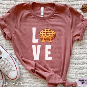 K&ouml;nnte beinhalten: Ein T-Shirt in der Farbe Heide-Mauve mit einer wei&szlig;en Grafik einer Waffel und dem Wort "LOVE".