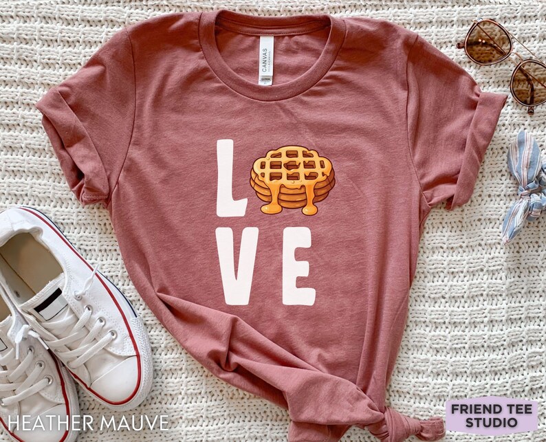 K&ouml;nnte beinhalten: Ein T-Shirt in der Farbe Heide-Mauve mit einer wei&szlig;en Grafik einer Waffel und dem Wort "LOVE".