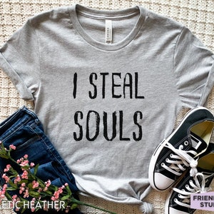 以下が含まれることがあります： 黒い文字で「I STEAL SOULS」とプリントされたグレーのTシャツです。