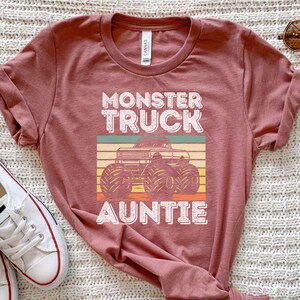 May include: A maroon t-shirt with a vintage-style graphic of a monster truck and the text "Monster Truck Auntie".