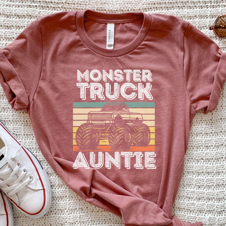 May include: A maroon t-shirt with a vintage-style graphic of a monster truck and the text "Monster Truck Auntie".