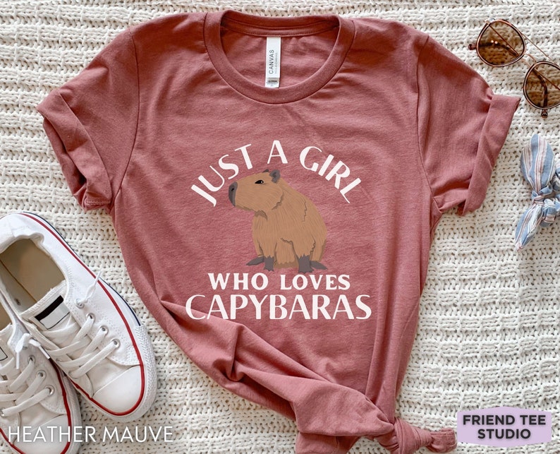 May include: A heather mauve t-shirt with the text "Just a girl who loves capybaras" and a cartoon image of a capybara.
