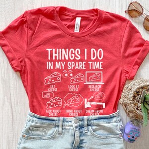 Puede incluir: Camiseta roja con un gr&aacute;fico blanco que dice "Cosas que hago en mi tiempo libre" y enumera actividades relacionadas con el queso. Las actividades incluyen comer, mirar, investigar, hablar, pensar y so&ntilde;ar con queso.