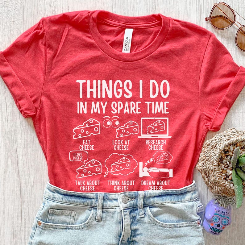 Puede incluir: Camiseta roja con un gr&aacute;fico blanco que dice "Cosas que hago en mi tiempo libre" y enumera actividades relacionadas con el queso. Las actividades incluyen comer, mirar, investigar, hablar, pensar y so&ntilde;ar con queso.