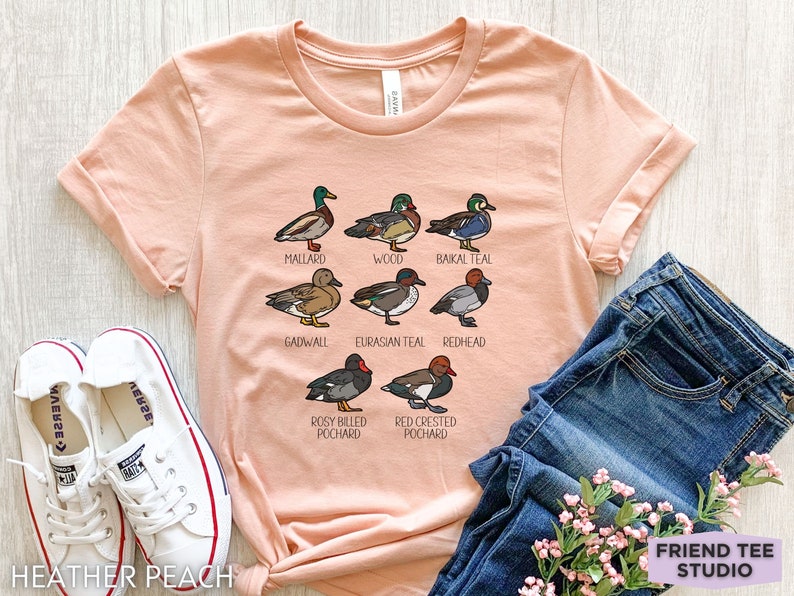 Peut inclure: Un t-shirt &agrave; manches courtes couleur p&ecirc;che avec une impression graphique de huit esp&egrave;ces de canards diff&eacute;rentes, accompagn&eacute;es de leurs noms : Mallard, Wood, Baikal Teal, Gadwall, Eurasian Teal, Redhead, Rosy Billed Pochard et Red Crested Pochard.