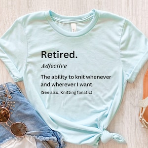 Puede incluir: Camiseta azul claro con el texto "Retired. Adjective: The ability to knit whenever and wherever I want. (See also: Knitting fanatic)". La camiseta est&aacute; anudada en la parte inferior.