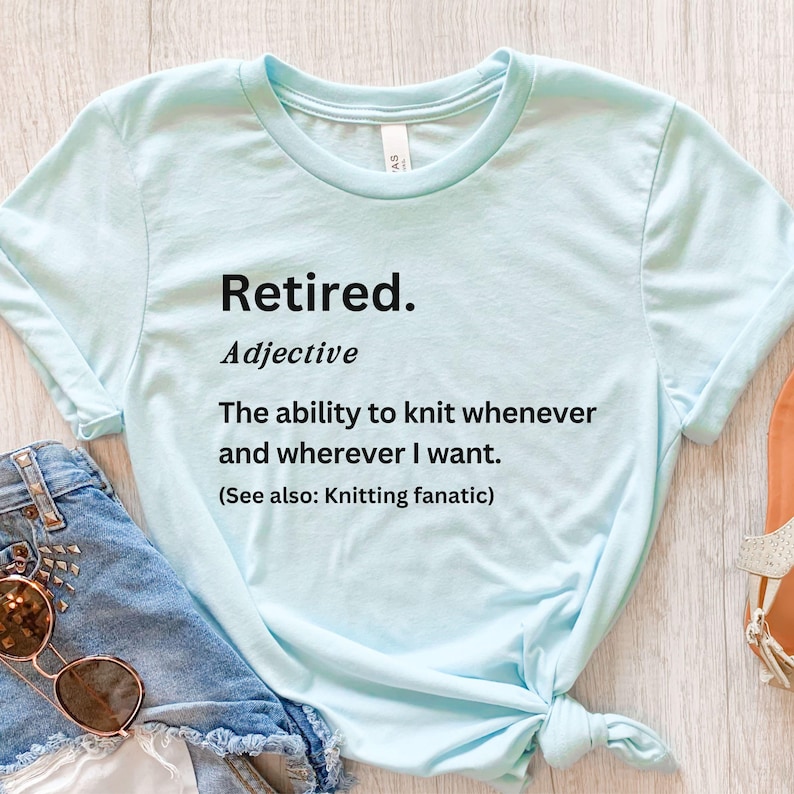 Puede incluir: Camiseta azul claro con el texto "Retired. Adjective: The ability to knit whenever and wherever I want. (See also: Knitting fanatic)". La camiseta est&aacute; anudada en la parte inferior.