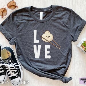 Op de afbeelding: Donkergrijs heather t-shirt met een witte afbeelding van een dumpling met eetstokjes en het woord "LOVE".