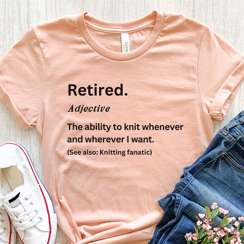Puede incluir: Una camiseta de color melocot&oacute;n con la palabra "Retired" impresa en negro, seguida de una definici&oacute;n. La definici&oacute;n dice: "La capacidad de tejer cuando y donde quiera". La camiseta se combina con vaqueros azules y zapatillas blancas.