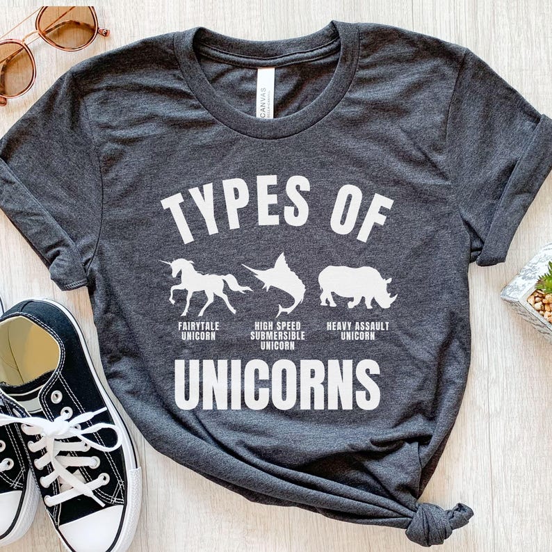 May include: A dark gray t-shirt with the text "TYPES OF UNICORNS" in white.  The shirt features three white silhouettes of unicorns: a fairytale unicorn, a high-speed submersible unicorn, and a heavy assault unicorn.