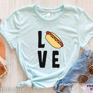 May include: A light blue t-shirt with the word "LOVE" in black letters. The "O" is replaced with a cartoon hot dog with mustard and ketchup.