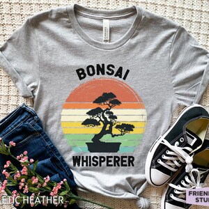 May include: A gray t-shirt with a vintage-style graphic of a bonsai tree and the text "Bonsai Whisperer".